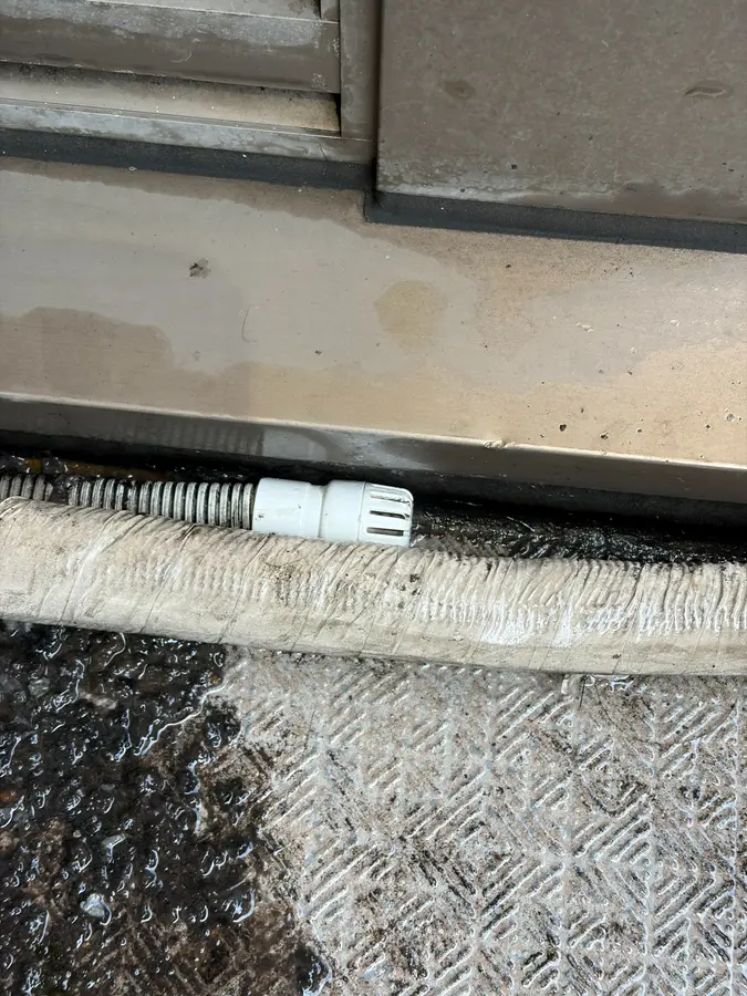 防虫キャップの付いたドレンホースの出口と、黒くにごった水