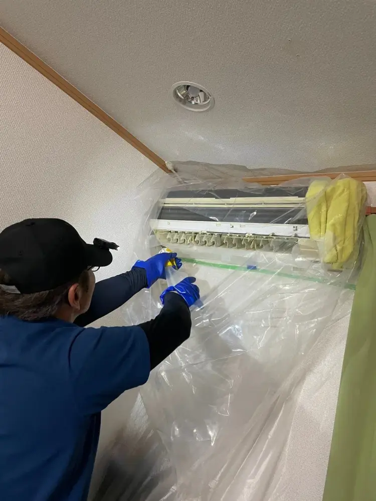 養生したエアコンに洗剤を吹きかけている作業風景